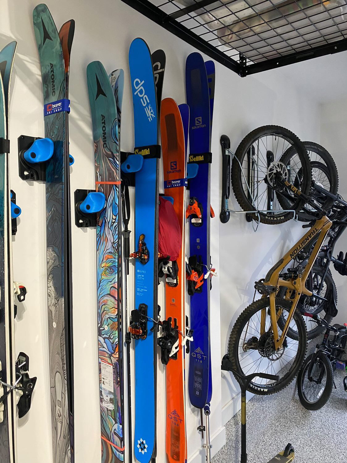 Five pairs of skis neatly stored on a wall using Gravity Grabber racks, each held securely by wide padded arms to keep them organized and off the floor.