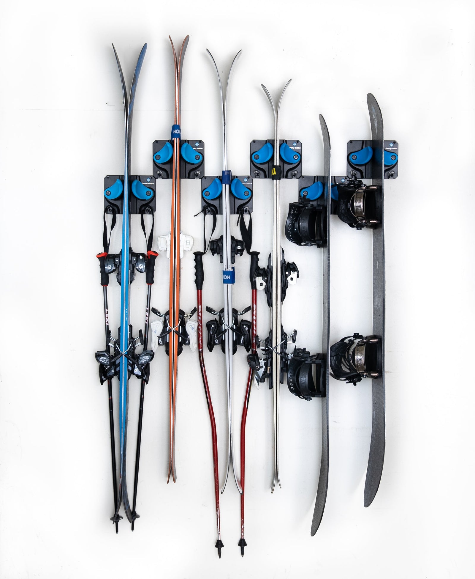 4 sets of skis and 2 snowboards hang in six gravity grabbers that are offset from one another.