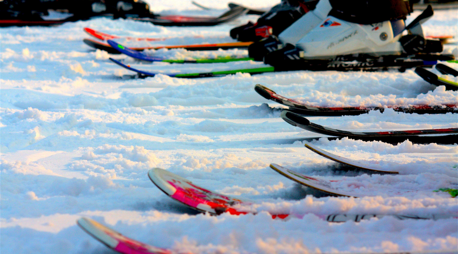 4 pairs of skis are in the snow as if the wearers are standing next to each other. One pair of white ski boots can be seen clipped in to one of the pairs of skis. The photo features the ski rocker.