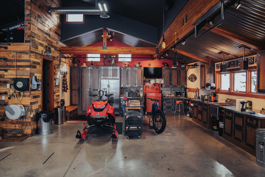 The image shows an organized garage. In the wooden lined, metal garage, there is a snowmobile and tools. Hanging on the walls are Gravity Grabbers, an innovative ski and storage rack. 