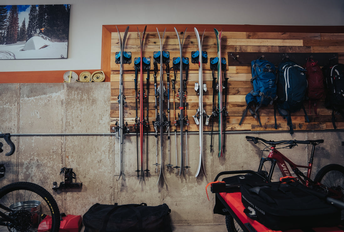 Garage wall with multiple pairs of skis neatly stored in Gravity Grabber wall racks alongside backpacks, a mountain bike, and outdoor gear.