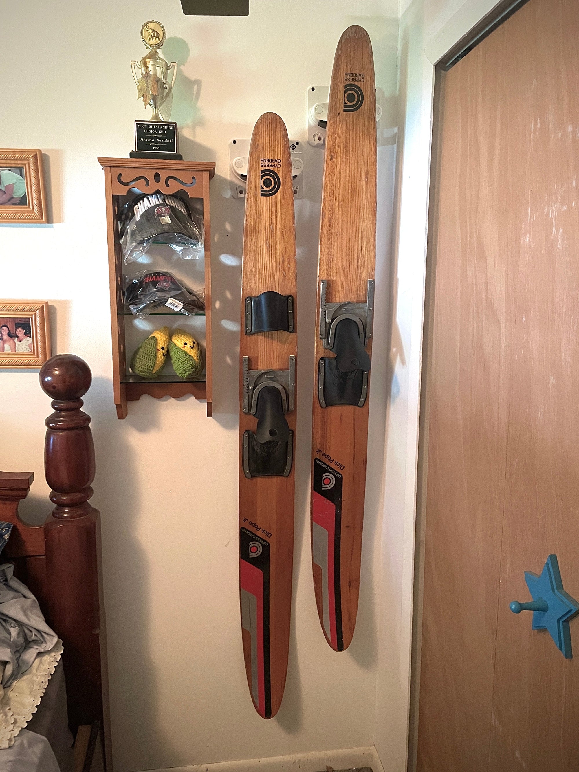 Waterskis hang in a Gravity Grabber indoors next to a bed. 