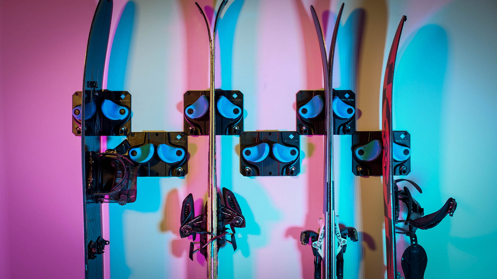 Five pairs of skis neatly stored on a wall using Gravity Grabber racks, each held securely by wide padded arms to keep them organized and off the floor.